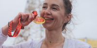 На изображении спортсменка символически "пробует на зуб" медаль за участие в полумарафоне и улыбается, Изображение. - Правительство Челябинской области