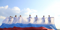 На изображении семь человек в белых рубашках стоят на фоне российского флага под голубым небом с облаками., Изображение. - Правительство Челябинской области