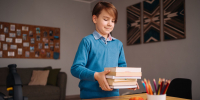 first_grade_boy_studying_home_holding_bunch_books_getting_ready - Новый Компаньон
