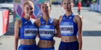 Три женщины в спортивной форме синего цвета стоят рядом друг с другом на улице. На заднем плане видны разноцветные конструкции и люди. Автор фото - Евгений Шерягин, оргкомитет соревнований - Коркинский муниципальный округ