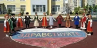 Дети в национальных костюмах стоят на школьном дворе, держась за руки перед нарисованным на асфальте сердцем с надписью «Здравствуйте». - Министерство образования и науки