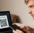 Мужчина держит смартфон рядом с ноутбуком, на экране которого открыт QR-код для оплаты - 168.Ru