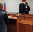 Мужчина стоит перед судьёй, читающей документ у стола в зале суда с российским флагом и гербом. - 168.Ru