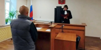 Мужчина стоит перед судьёй, читающей документ у стола в зале суда с российским флагом и гербом. - 168.Ru