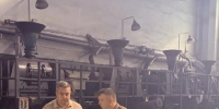 Двое мужчин стоят в производственном цеху завода и обсуждают документы на фоне крупного промышленного оборудования и ёмкостей/ковшей для металла. - 168.Ru