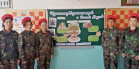 На фото — группа подростков в камуфляжной форме и красных беретах позирует перед школьной стендовой композицией, посвящённой Нурмагомеду Хаджимагомедову и Василию Марзоеву, с инфографикой о ценностях и качествах личности. - Министерство образования и науки