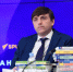 мужчина в тёмном костюме сидит за столом на фоне баннера «РИА Новости», перед ним несколько стопок учебников и микрофон - 168.Ru