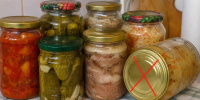 Несколько стеклянных банок с домашними консервами (солёные огурцы, овощи, мясной паштет, квашеная капуста); одна банка лежит на боку с красным крестом на крышке. - 168.Ru