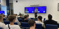 На фото — лекция «Как распознать мошенника»: спикер у экрана выступает перед аудиторией из молодых слушателей в лекционном зале. - Министерство образования и науки
