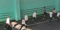 Школьники в спортивном зале выполняют легкоатлетические упражнения/разминку; видны зелёно‑жёлтые стены, скамьи и радиаторы. - 168.Ru