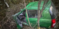 Сильно поврежденный зеленый автомобиль среди деревьев и кустарника - 168.Ru