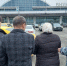 Сотрудница ФССП ведёт задержанную женщину и ещё несколько человек на парковке на фоне здания аэропорта с надписью «ВНУКОВО» - 168.Ru
