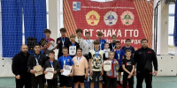 Группа юных спортсменов и два тренера в спортивном зале: медали на шее, дипломы в руках, победный подиум с цифрами 1–3 на фоне баннера. - 168.Ru