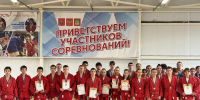 На фото — группа юных самбистов в красных кимоно с медалями и грамотами на фоне баннера «Приветствуем участников соревнований!» в спортивном зале. - Министерство образования и науки