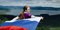 Молодая женщина на смотровой площадке: она стоит вполоборота, улыбается и держит развёрнутый российский триколор, Изображение. - Правительство Челябинской области