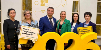 На фото — группа из шести человек на фоне декораций с жёлтыми цифрами «2026», двое участников держат таблички с лозунгами «Ямал — территория сильных!» и «Будущее начинается с нас!». - Министерство образования и науки
