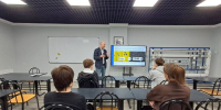 В учебной аудитории преподаватель проводит занятие для группы студентов: на экране — презентационный слайд с техническими данными, справа — демонстрационный стенд с инженерным оборудованием. - Министерство образования и науки