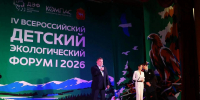 На сцене IV Всероссийского детского экологического форума 2026 года мужчина в костюме выступает с речью в микрофон, рядом стоят женщина в белом костюме с папкой и мужчина в пиджаке, на фоне — тематический декор с пейзажем, птицами и логотипом мероприятия. - Министерство образования и науки