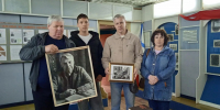 Четверо человек в музейном интерьере держат в руках две рамки с чёрно‑белыми фотографиями (одна большая портретная), на стенах — музейные стенды и экспонаты. - 168.Ru
