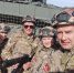 Семья Гордиенко в камуфляжной форме, шлемах и тактическом снаряжении позирует на фоне танка, один из мужчин держит автомат, все улыбаются. - Коркинский муниципальный округ
