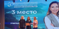 На сцене три женщины — участницы IX Всероссийского конкурса «Учитель‑дефектолог России — 2026»: одна из них держит диплом за 3‑е место в номинации «Дефектолог года», другая — букет, на фоне — экран с оформлением конкурса и портрет участницы. - Министерство образования и науки