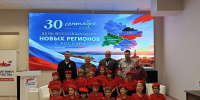 На фото — группа детей в красных футболках и черных брюках с подарочными пакетами и взрослые на фоне баннера, посвящённого Дню воссоединения новых регионов с Россией (30 сентября 2026 года), с картой ЛНР, ДНР, Запорожской и Херсонской областей. - Министерство образования и науки