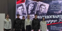Группа школьников/участников на сцене перед большим экраном с изображениями молодогвардейцев и надписями о «Молодой гвардии». - 168.Ru