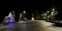 На фото — ночной мемориальный комплекс с памятными конструкциями, звездой с подсветкой, памятником и табличкой «Участникам специальной военной операции» в окружении деревьев и фонарей. - Коркинский муниципальный округ