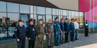 На фото группа сотрудников силовых структур и ведомств выстроилась в ряд перед современным зданием — рядом видны акустическая аппаратура и флагштоки, справа стоит женщина с микрофоном. - Коркинский муниципальный округ