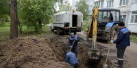 Рабочие роют траншею и ремонтируют подземную трубу рядом с многоквартирным домом; видны экскаватор и служебный автомобиль. - 168.Ru