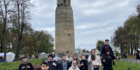 Группа школьников на экскурсии на фоне высокого каменного памятника с колонной и фигурой - 168.Ru