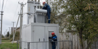 Два рабочих в касках обслуживают уличную трансформаторную подстанцию рядом с опорами линий и жилыми домами - 168.Ru