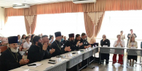 На фото — участники мероприятия в конференц‑зале: на переднем плане священнослужители за длинным столом, справа — светские участники, на столах — таблички с именами, смартфоны и документы. - Министерство образования и науки