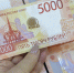 Рука держит купюру 5000 рублей на фоне нескольких таких купюр - 168.Ru