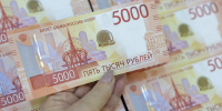 Рука держит купюру 5000 рублей на фоне нескольких таких купюр - 168.Ru