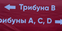 Красный баннер/плакат с белыми стрелками и указателями трибун: надпись «Трибуна В» и фрагмент «рибуны A, C, D» (навигация по трибунам стадиона). - 168.Ru
