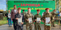 Юнармейцы-подростки в камуфляжной форме и красных беретах с грамотами стоят на сцене перед зелёным баннером с надписью «Зарница» и названием рубежа Василевского. - 168.Ru