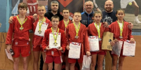 Группа юных самбистов в красной форме с медалями и грамотами в спортивном зале - 168.Ru