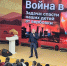 На фото мужчина в деловом костюме выступает на сцене перед аудиторией; на большом экране — слайд с заголовком «Война в тылу. Задача: спасти наших детей от вербовки» и тематическими изображениями. - Министерство образования и науки