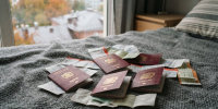 Несколько иностранных паспортов в бордовых обложках и билеты рассыпаны на сером покрывале - Newsroom24.Ru