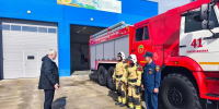 На изображении пожарная машина красного цвета рядом с синим зданием. Возле машины стоят три человека в форме. - Министерство гражданской обороны и чрезвычайных ситуаций