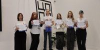 Шестеро молодых людей стоят с сертификатами в руках на фоне минималистичного интерьера с графическим декором. - Министерство образования и науки