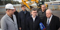 Несколько мужчин у строительной площадки: экскаватор JCB, временное ограждение стройплощадки и трибуны стадиона на заднем плане; микрофоны на переднем плане. - 168.Ru