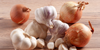 Pile of whole onions and garlic bulbs and cloves on a wooden table - Газета Восход