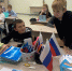 Младшие школьники в классе за партами во время занятия; на переднем плане учебники и распечатки, одна из которых — иллюстрация с ребёнком и мобильным телефоном/монстром. - 168.Ru