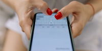 Пальцы с красным маникюром печатают сообщение на смартфоне в зелёном чехле - Newsroom24.Ru
