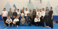Группа шестиклассников в школьном спортивном зале с инструктором-кинологом в форме и чёрной служебной собакой - 168.Ru