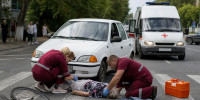 медики оказывают помощь пожилой женщине, лежащей на пешеходном переходе; рядом упавший велосипед, легковой автомобиль и скорая помощь - 168.Ru
