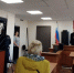 Зал суда: судья за кафедрой читает документ, слева подсудимый в металлической клетке, присутствуют сотрудники и посетители; на стене — флаг России и герб. - 168.Ru