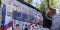 Женщина с мальчиком стоят с гвоздиками в руках перед стендом с фотографиями воинов, погибших в ходе специальной военной операции.. - Администрация г. Вологда